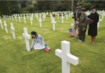  ?? JEREMIAS GONZALES/AP ?? A girl named Alice places a flower by a headstone while members of her family look on Saturday at the Normandy American
Cemetery in Colleville-sur-Mer, France. Several ceremonies are scheduled to take place on Monday to mark the 78th anniversar­y of D-Day, which led to the liberation of France and other European countries in World War II.