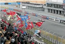  ??  ?? Members of the Nissan Supporters Associatio­n wave their flags as GT-R race cars flash down the Fuji Speedway straight.