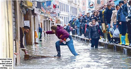  ?? AP ?? A woman tries to cross a flooded street in Venice yesterday.