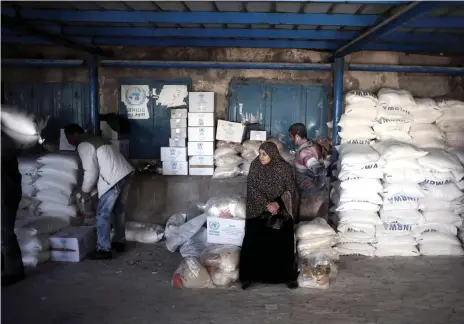  ?? AP ?? A Palestinia­n woman waits for food aid at a UN warehouse in the Shati refugee camp, Gaza, where many still need help to survive