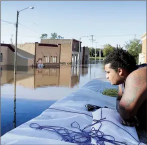  ?? AP/ CHARLIE NEIBERGALL ?? Cory Harrison stands at a fl ood wall Tuesday near businesses inundated by the rain- swollen Cedar River in Cedar Rapids, Iowa. An elaborate system of temporary fl ood walls put up over the weekend protected most homes and businesses in the city, but...