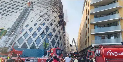  ??  ?? Firefighte­rs and people gather near the site of a fire that broke out in a building in Central Beirut yesterday.