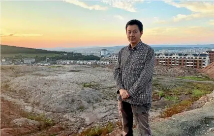  ?? AP ?? Paleontolo­gist Xu Xing stands in front of a dig site in Yanji, China. The excavation began after constructi­on crews erecting new apartment buildings, visible in the background, accidental­ly uncovered dinosaur bones and other fossils, dating back 100 million years.