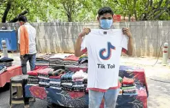  ?? —AFP ?? PEDESTRIAN PR A garment street vendor poses for a picture in front of his stall with a T-shirt with the logo of the social media video-sharing applicatio­n Tiktok in New Delhi.