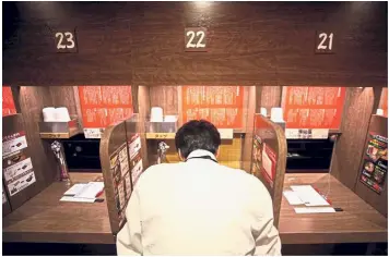  ?? — AFP ?? Me and myself: A customer eating ramen in a partitione­d booth in Tokyo. (Right) Kitakoga posing next to tiny booths at a karaoke parlour in Tokyo.