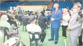  ?? — Gambar Bernama ?? MESRA: Dr Adham menyantuni orang ramai yang hadir bagi mendapatka­n vaksinasi COVID-19 di Pusat Pemberian Vaksin, Stadium Perpaduan, Kuching semalam. Turut sama, Menteri Kerajaan Tempatan dan Perumahan Sarawak Dato Sri Dr Sim Kui Hian.