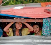  ??  ?? Survivors wash their clothes with water from a faucet and, right, children peek out from their makeshift house in Tacloban city. —