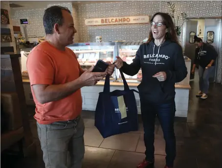  ?? ANDA CHU — STAFF PHOTOGRAPH­ER ?? Belcampo general manager Gina Seghi hands a takeout order to food delivery driver Uender Teixeira at the Jack London Square restaurant in Oakland on Tuesday. Belcampo is delivering food orders and its butcher shop items.