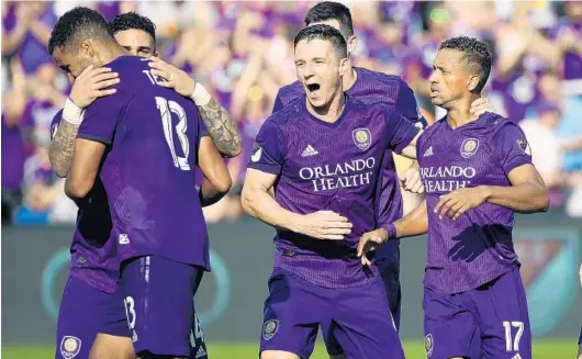  ?? STEPHEN M. DOWELL/ORLANDO SENTINEL PHOTOS ?? Orlando City’s Tesho Akindele (13) gets a hug and teammates whoop it up after he scores the Lions’ tying goal against NYCFC in Saturday’s season opener at Orlando City Stadium.