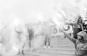  ??  ?? Tunisians carry flares shout slogans against the government in Tunis, during a demonstrat­ion over price hikes and austerity measures. — AFP photo