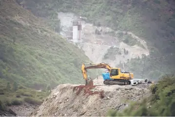  ?? — AFP photos ?? This picture taken on May 28 shows a constructi­on site for a road near the Lianghekou dam near Hekou in Sichuan province. (Left) A man sitting on a wall next to the constructi­on site of the Lianghekou dam near Hekou in Sichuan province. Towering walls...