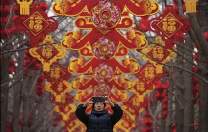  ?? ASSOCIATED PRESS ?? A woman takes a picture on Sunday of red lanterns and decoration­s on display along the trees ahead of the Chinese Lunar New Year at Ditan Park in Beijing.