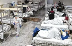  ?? CHINATOPIX ?? A medical worker in a protective suit walks by coronaviru­s patients at a temporary hospital in an exhibition center in Wuhan, China. The government reported 73 more deaths and announced that patients would begin taking a new antiviral drug.