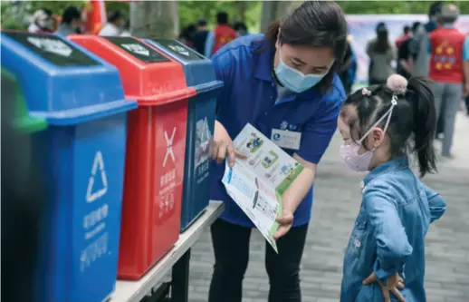  ??  ?? A community worker shows a girl trash sorting rules in a residentia­l community in Beijing on May 23