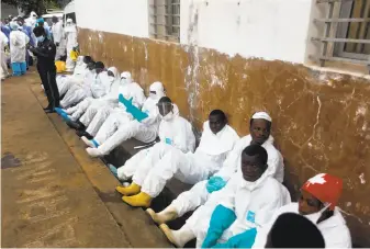  ?? Saidu Bah / AFP / Getty Images ?? Burial team members, some of the 600 the government has hired, rest outside a hospital in Freetown, Sierra Leone, where 350 people died after torrential rains caused massive mudslides.