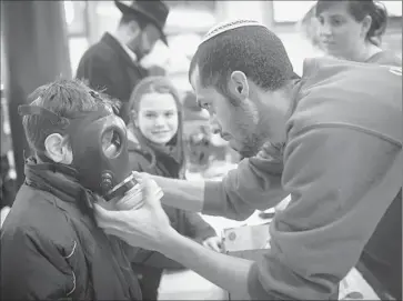  ?? Photog raphs by Oren Ziv
Getty Images ?? AN ISRAELI postal worker shows a child how to don a gas mask at a distributi­on station in Pisgat Zeev, East Jerusalem. Israelis are bracing for attacks after Israel struck targets outside Damascus, the Syrian capital.