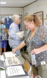 ?? Lynn Atkins/The Weekly Vista ?? Kathy Cox looks through one of the many scrapbooks on display at the Bella Vista History Museum during the annual open house last week. Cox promised to donate some family items that help tell the history of one marketing effort devised by John Cooper...