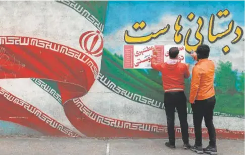  ?? // REUTERS ?? Dos hombres pegan carteles de propaganda electoral en una pared de Teherán