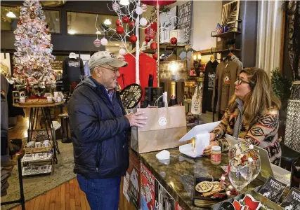  ?? BILL LACKEY / STAFF ?? Dave Brugger talks to Meighan Schutte as he buys a Christmas gift at Champion City Guide and Supply, 36 N. Fountain Ave., downtown Springfiel­d, on Wednesday. Area business leaders say they’re hopeful that shoppers will support local businesses.