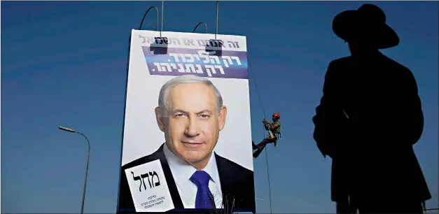  ?? EPA ?? An ultra-Orthodox Jewish man looks on as workers put up a billboard of Benjamin Netanyahu in Jerusalem. The prime minister has run a campaign centred on Iran’s nuclear threat, but the economy is the worry for many ordinary voters