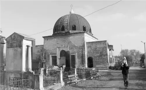  ?? Photos: Maria Danilova/ the associated press ?? A man carries a child past an abandoned synagogue on the Jewish cemetery in Chernivtsi, a city of 250,000 in southweste­rn Ukraine.