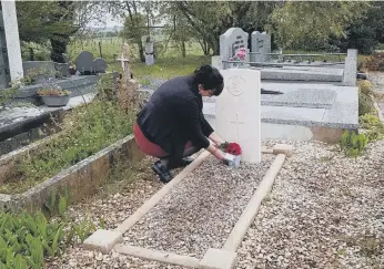  ??  ?? Regine places a small bunch of flowers on the grave of Private Thomson.