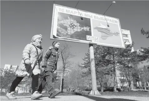  ?? VIKTOR DRACHEV/Getty Images ?? Children walk past a billboard sign in Sevastopol on Thursday that reads, ‘On March 16 we will choose either ... or ...’ and depicting Crimea with a swastika and covered in barbed wire, left, and Crimea draped by a Russian flag design. Less than three...