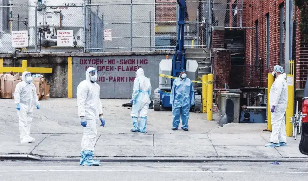  ?? Agence France-presse ?? ↑
Medical workers wearing personal protective gear work to remove a body at a hospital in New York.