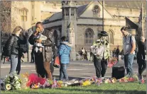  ?? AP PHOTO ?? A police officer places flowers as a man gestures beside floral tributes to victims of Wednesday’s attack, on Parliament Square outside the Houses of Parliament in London, Friday.