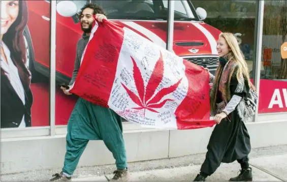  ?? GRAHAM HUGHES — THE CANADIAN PRESS VIA AP ?? People hold up a Canadian flag with a marijuana logo on it outside a government cannabis store in Montreal, Wednesday. Canada became the largest country with a legal national marijuana marketplac­e as sales began early Wednesday.