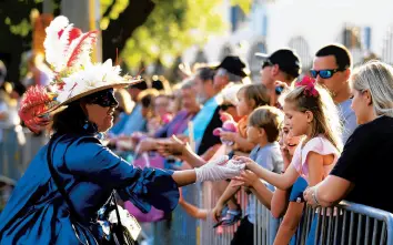  ?? GERALD HERBERT/AP ?? A woman dressed in period costume hands a trinket to a child during a parade dubbed“Tardy Gras,”to compensate for a canceled Mardi Gras due to the COVID-19 pandemic, on Friday in Mobile, Alabama.