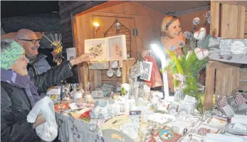  ?? FOTO: ISABEL KUBETH DE PLACIDO ?? Während Waltraud Hattinger (in der Bude) begeistert ist vom Bodolzer Adventssta­delmarkt, begeistert ihre Papierkuns­t die Besucher, wie hier Adelheit Karg und Hubert Mark.