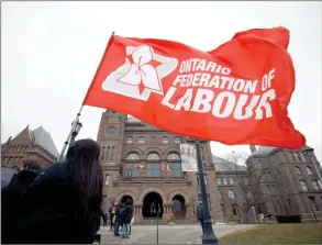 ?? The Canadian Press ?? A person carries the Ontario Federation of Labour flag as a group advocating for provincial­ly mandated paid sick days for workers participat­ed in a ‘die-in’ rally outside Queens Park in Toronto.