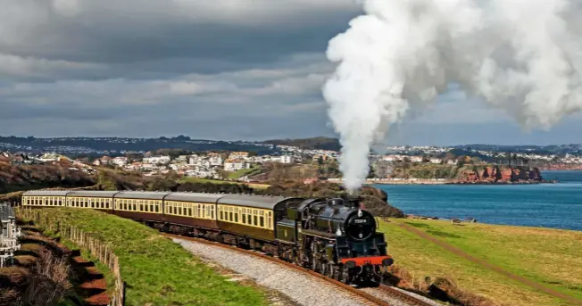  ??  ?? A steam train climbs away from Paignton, snaking along the coastline as it heads on to Dartmouth. ›