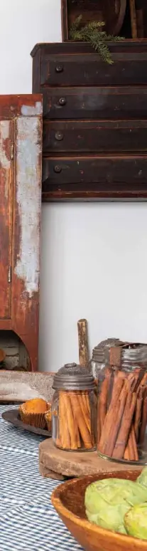  ??  ?? To create an authentic primitive vibe near the kitchen eating area, Edith gathered a variety of antique and distressed woodenware­s. A simple dining table and chairs balance the antique dry sink accented with signage, firkins, dough bowls and primitive plates. Nearby, a ladder leans against the wall next to an old wooden mortar and pestle, while two hanging cupboards complete the monochroma­tic theme.