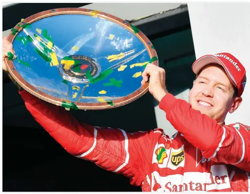  ??  ?? Ferrari’s German driver Sebastian Vettel celebrates with the winner’s trophy on the podium following his victory in the Australian Grand Prix in Melbourne on Sunday. (AFP)