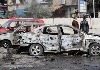  ?? — AFP ?? Syrian men stand next to a damaged car at the site of a suicide attack on a police officers’ club in the Masaken Barzeh district of the capital Damascus on Tuesday. Nine people died in the attack.