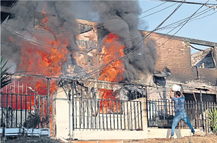  ?? ?? A resident desperatel­y tries to halt the spread of flames at a property in Viña del Mar