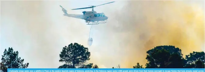  ??  ?? A helicopter drops water over a wildfire in Pinet, in the eastern Spanish region of Valencia, yesterday. In the Valencia region some 2,500 people were driven from their homes overnight to escape flames that have already swept across around 1,000 hectares, as fire crews struggled to bring the fires under control. — AFP