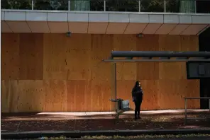  ?? (AP/Marcio Jose Sanchez) ?? A woman waits at a bus stop Monday in front of a boarded-up storefront in Portland, Ore., as business owners prepare for possible unrest today.