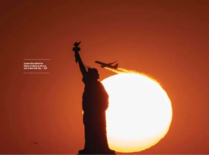  ?? — AFP ?? A plane flies behind the Statue of Liberty as the sun sets in New York City.