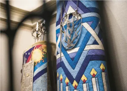  ?? TELECHAN/POST-TRIBUNE KYLE ?? Torahs wrapped in ornately knit decoration­s are displayed behind a metal sculpture of the tree of life at Temple Israel in Gary on April 10.