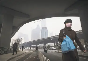  ?? Kevin Frayer / Getty Images 2016 ?? A Chinese woman wears a mask as she walks down a street on a polluted day in Beijing last month.