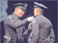  ??  ?? Rio Rancho police officer Gabe Sanchez, left, pins a badge on his twin brother, Anthony Sanchez, during the graduation ceremony at the Albuquerqu­e Convention Center.
