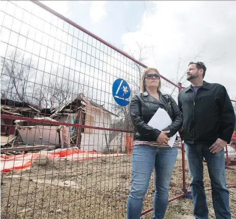  ?? KAYLE NEIS ?? Shannon Vinnish and Daniel Gerle stand outside the home at Avenue B North and 34th Street West in Saskatoon that has been left partly demolished since last fall with asbestos warnings on the fence. The city says it will resume demolition next week.