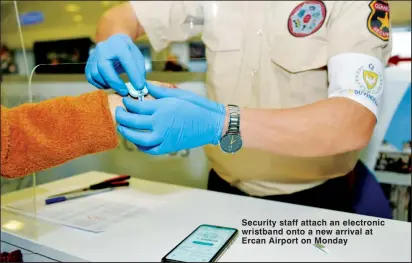  ??  ?? Security staff attach an electronic wristband onto a new arrival at Ercan Airport on Monday