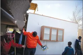  ?? AP/DAVID GOLDMAN ?? Granadas Baker (second from left) passes a family photo Monday to his daughter Kiara Slater (left) while holding up an unsteady wall with son Granadas Jr. 18, (right) as his other son Cameron, 11, looks on. The family was retrieving personal items from the damaged home where they survived a tornado a day earlier in Beauregard, Ala.