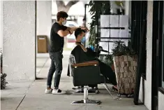  ?? AP Photo/ Jae C. Hong ?? ■ Hairstylis­t Travis Vu gives a haircut to Minh Dao at his outdoor hair salon Wednesday in Fountain Valley, Calif. The worsening COVID-19 pandemic threatens to choke off the U.S. economy’s fragile recovery and turn what some investors hoped would be a sprint back to normal into a long,
hard slog.