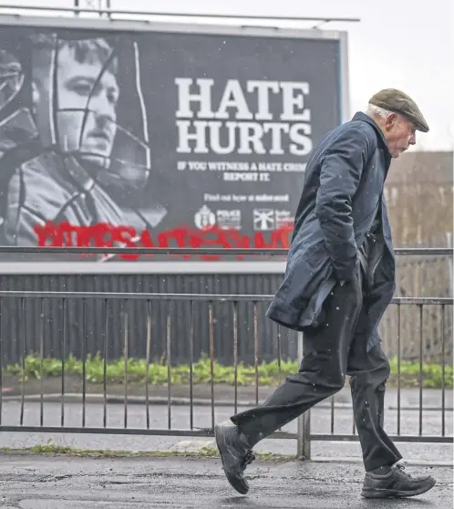  ?? ?? A member of the public walks past a hate crime billboard in Glasgow. The ‘Hate Hurts’ campaign featured the slogan ‘if you witness a hate crime, report it’