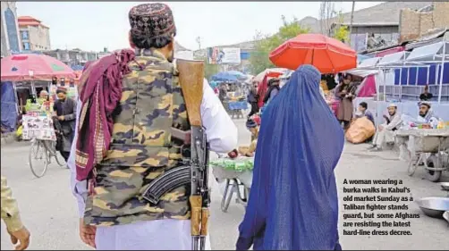 ?? ?? A woman wearing a burka walks in Kabul’s old market Sunday as a Taliban fighter stands guard, but some Afghans are resisting the latest hard-line dress decree.